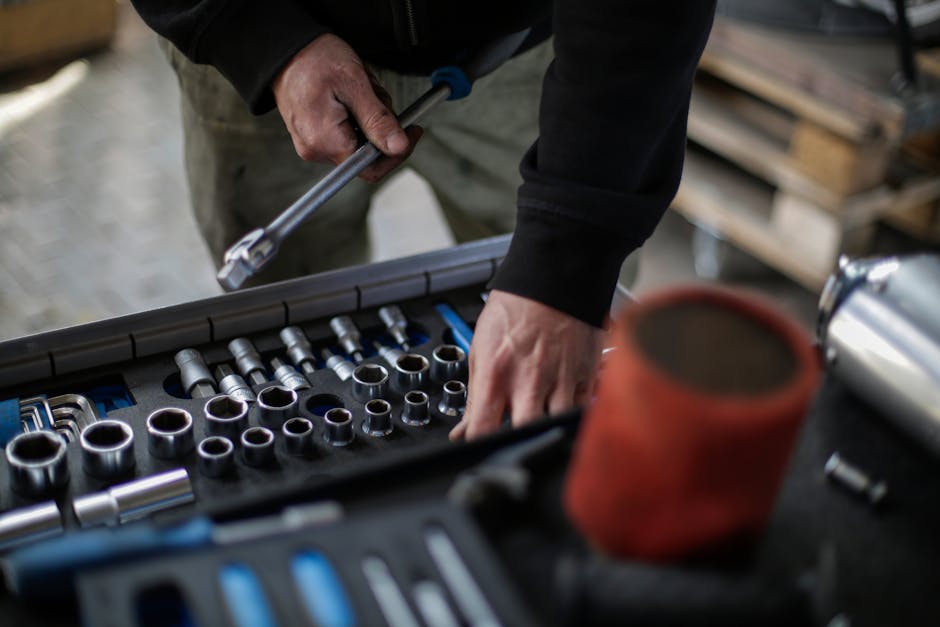 From above view of crop unrecognizable mechanic in workwear choosing metal sockets for ratchet while repairing vehicle in modern workshop